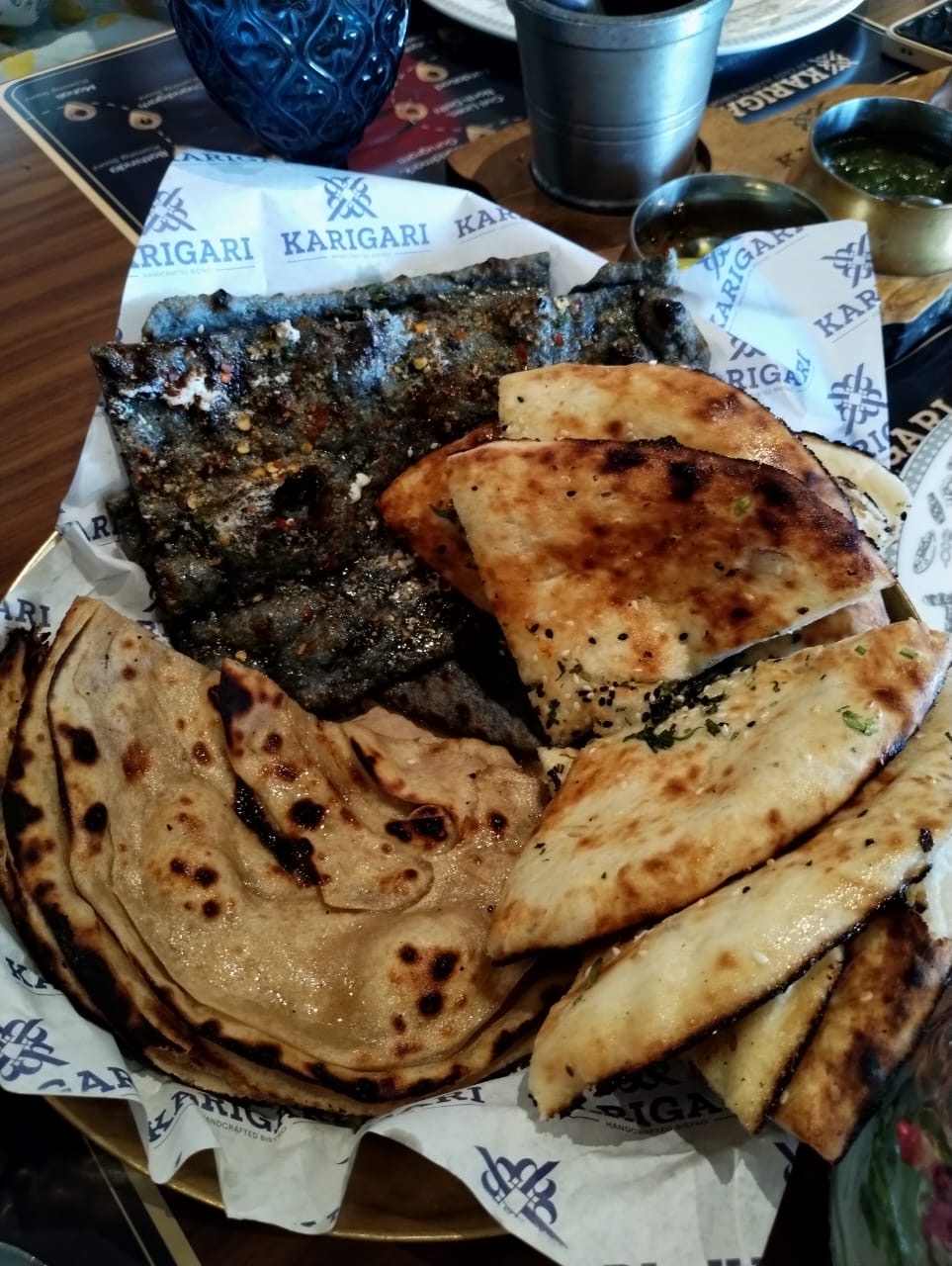 Assorted flatbreads — naan, paratha and a dark seasoned bread — on branded paper